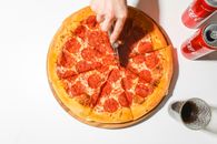 Person Slicing A Pizza With A Pizza Cutter