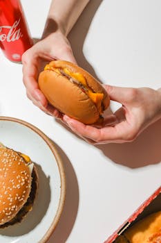 Tasty cheeseburger held in hands with a soft drink. Perfect for fast food cravings.