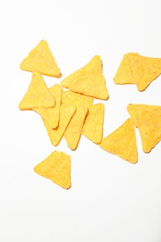 A group of crunchy yellow tortilla chips on a white surface, ideal for snack-themed projects.