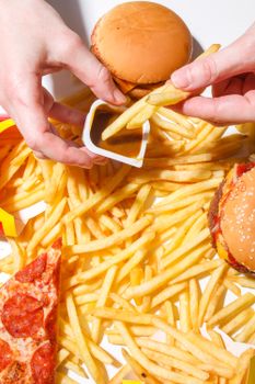 Close-up of hands holding fries over burgers and pizza, showcasing classic fast food items.