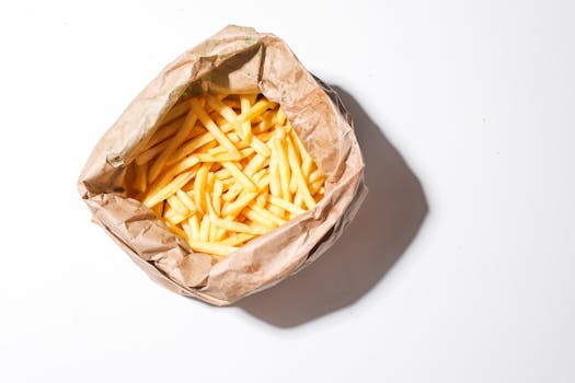 Top view of crispy French fries in a brown paper bag on a white background.