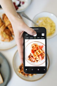 A hand taking a photo of waffles with a smartphone at breakfast.
