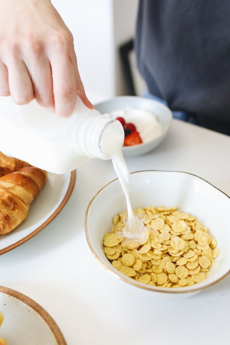 Person Pouring A Milk Into The Bowl Of Cereal