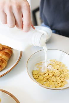 Hand pouring milk into a bowl of cereal for a breakfast setting.