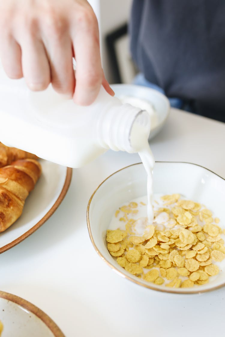 Person Pouring A Milk Into The Bowl Of Cereal