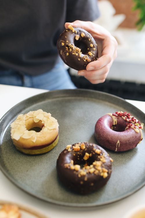 Free Close-up of a hand holding a gourmet donut on a tray with various flavored donuts. Stock Photo