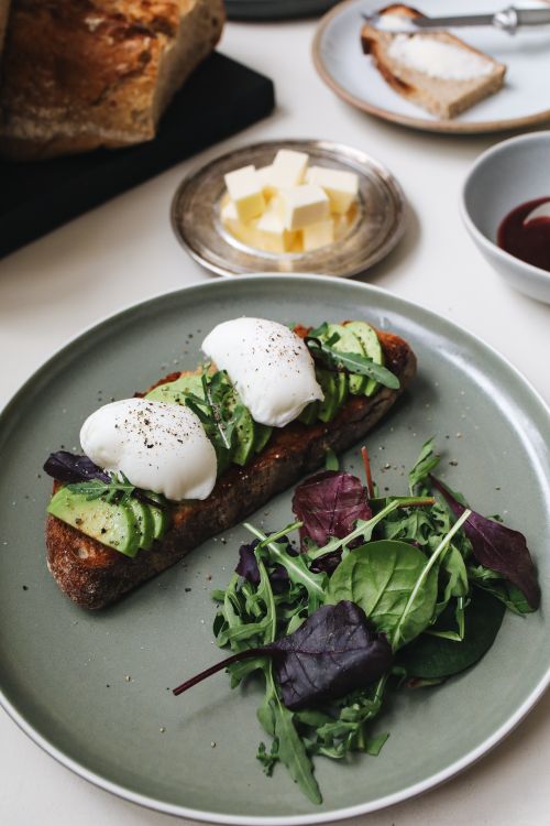 Free Gourmet avocado toast topped with poached eggs and fresh greens on a ceramic plate. Stock Photo
