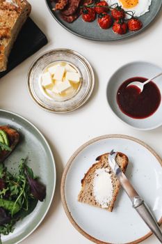 A top-down view of a breakfast spread featuring fresh bread, butter, eggs, and salad.