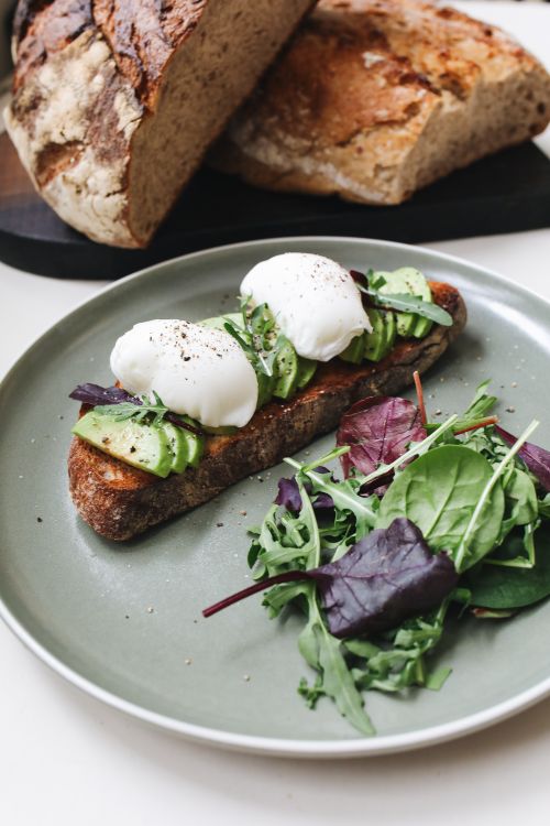 Free Delicious avocado toast with poached eggs and fresh greens on a plate, perfect for breakfast. Stock Photo