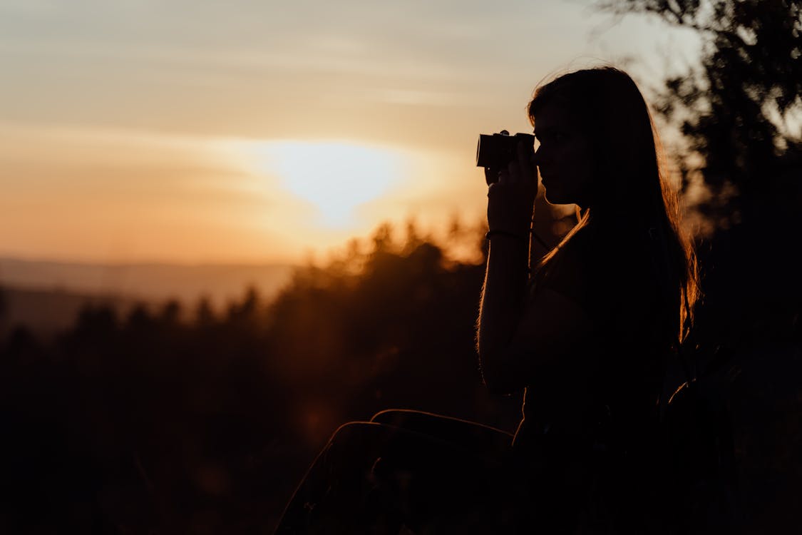 Woman Holding a Black DSLR Camera during Sunset