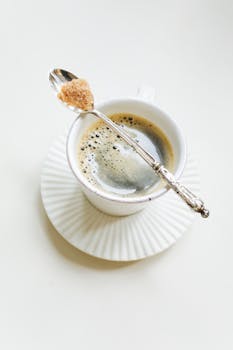 A close-up of coffee in a white cup with a spoon and sugar cube on a saucer.