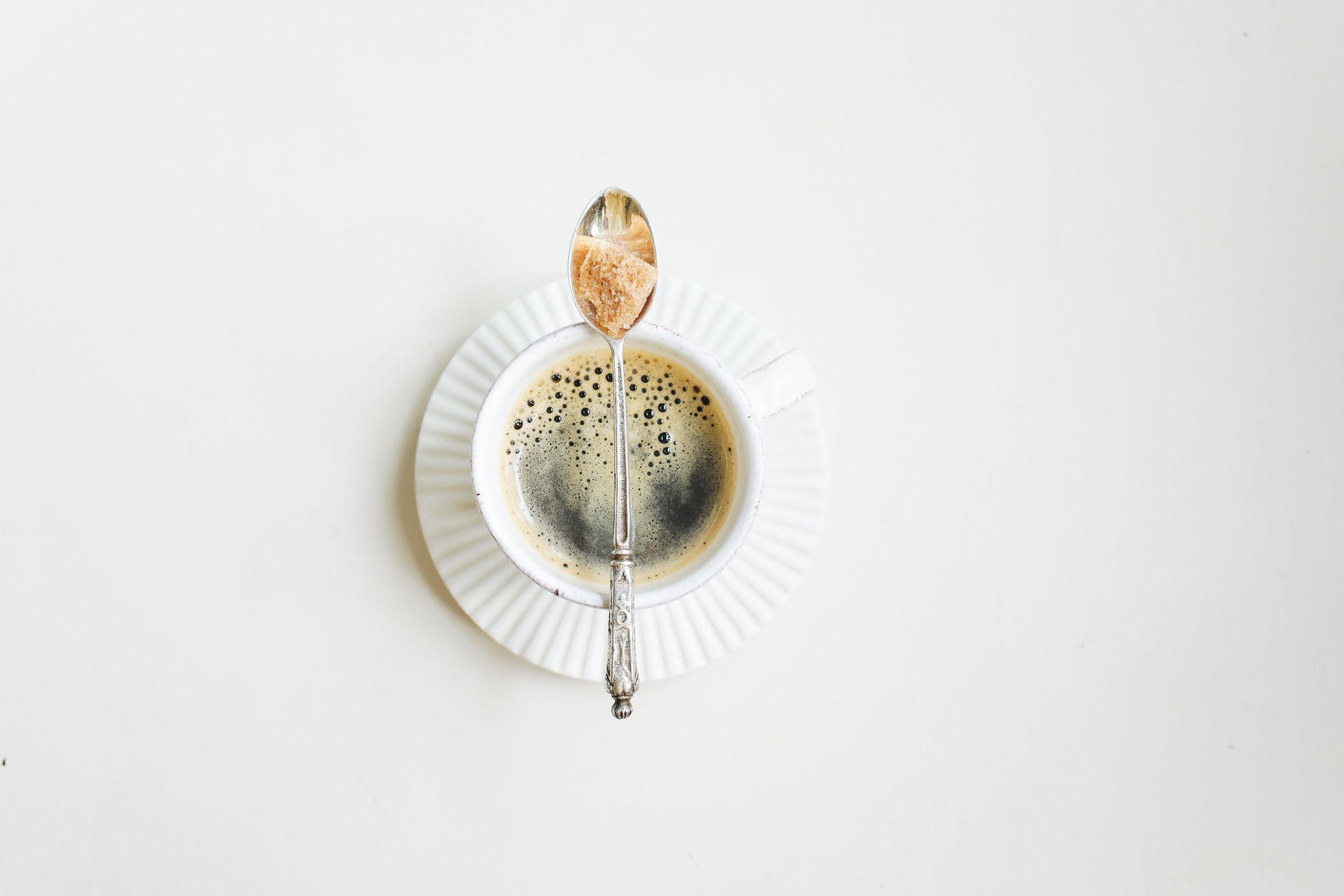 Elegant minimalist photo of a coffee cup with sugar spoon on a white background.