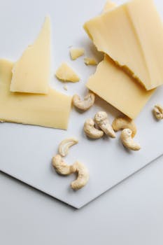 Delicious cashew nuts paired with gourmet cheese slices on a white surface.
