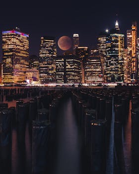 Dramatic night view of New York skyline with illuminated skyscrapers and a full moon.