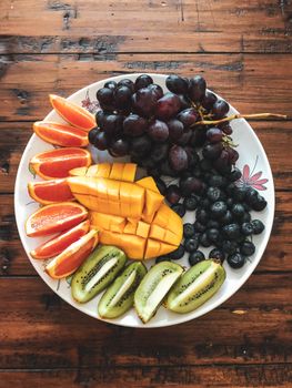 A colorful fruit platter featuring grapes, mango, kiwi, and oranges on a wooden table.