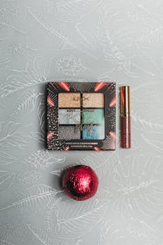 Vibrant eyeshadow palette with lip gloss and festive ornament on floral pattern.