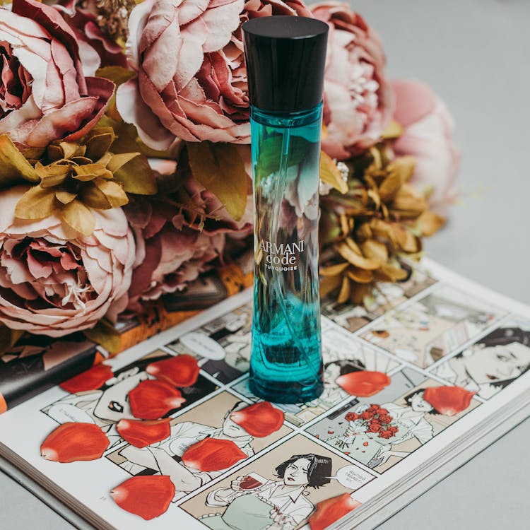 Blue Perfume Bottle On A Book Beside Flowers