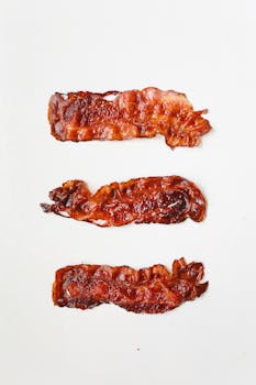 Three crispy bacon strips displayed on a clean white background, ideal for food enthusiasts.