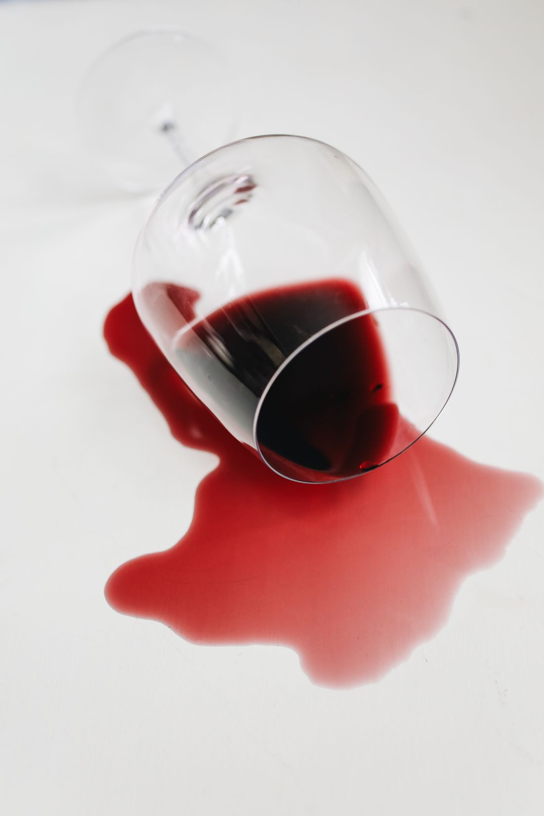 Red wine spilling from a tipped glass onto a white surface