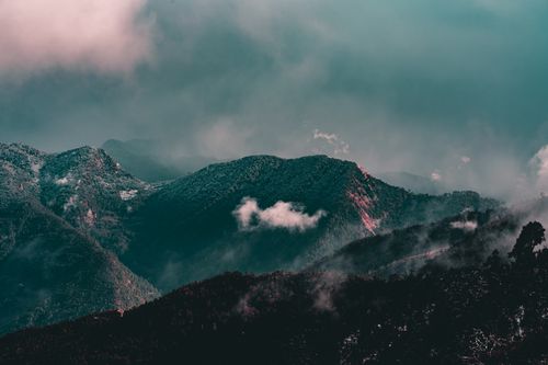 Free Majestic landscape of mountains covered with trees with snowy peaks under floating clouds on foggy day Stock Photo
