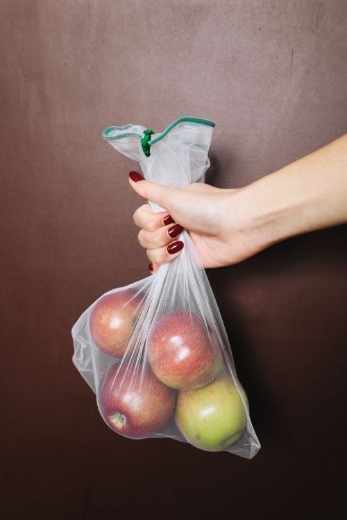 Free A close-up of a hand holding a plastic bag containing fresh red and green apples. Stock Photo