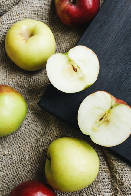 Whole and halved green apples displayed on a gray textured surface`