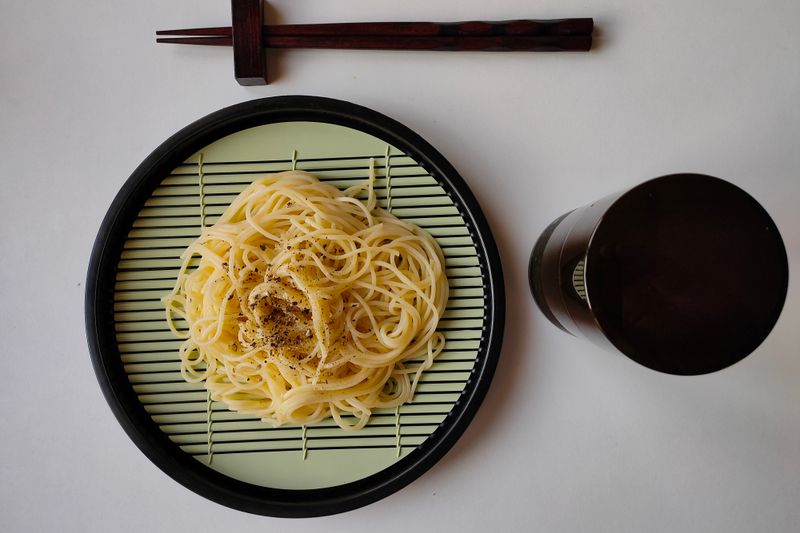 Spaghetti served on a round plate with chopsticks, showcasing an Asian fusion dining experience.