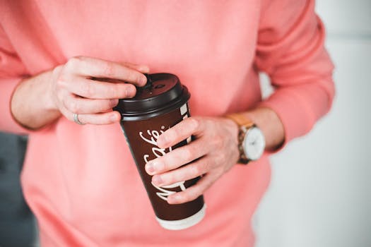 A person wearing a pink sweater holding a takeaway coffee cup. Perfect for lifestyle or coffee themes.