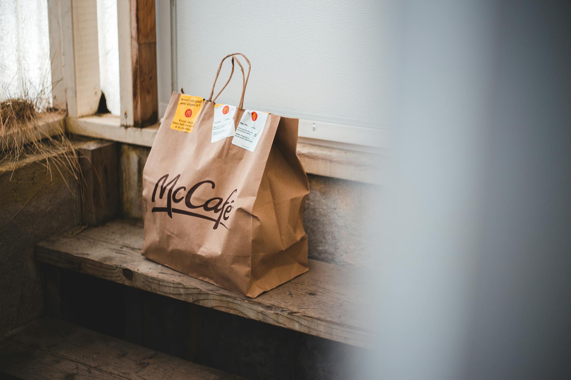 A McCafé paper bag resting on a rustic wooden bench, captured indoors with soft lighting.