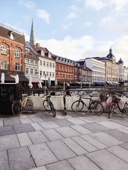 A lively urban street scene in Aarhus, Denmark with bicycles parked along the sidewalk.