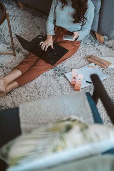 Woman working from home on a laptop, sitting on a cozy rug with a phone and colorful notes around.
