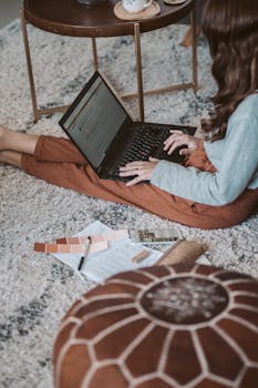 Woman working remotely from home on a laptop, surrounded by design samples.