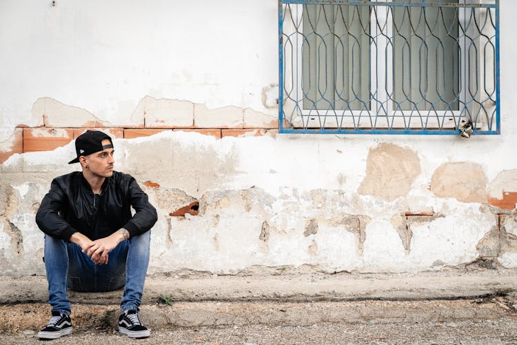 Man Sitting By Neglected House