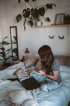 Woman enjoying remote work from home with laptop in a cozy bedroom.