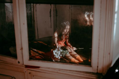 Free Moody indoor portrait of a woman in reflection holding flowers by a window. Stock Photo