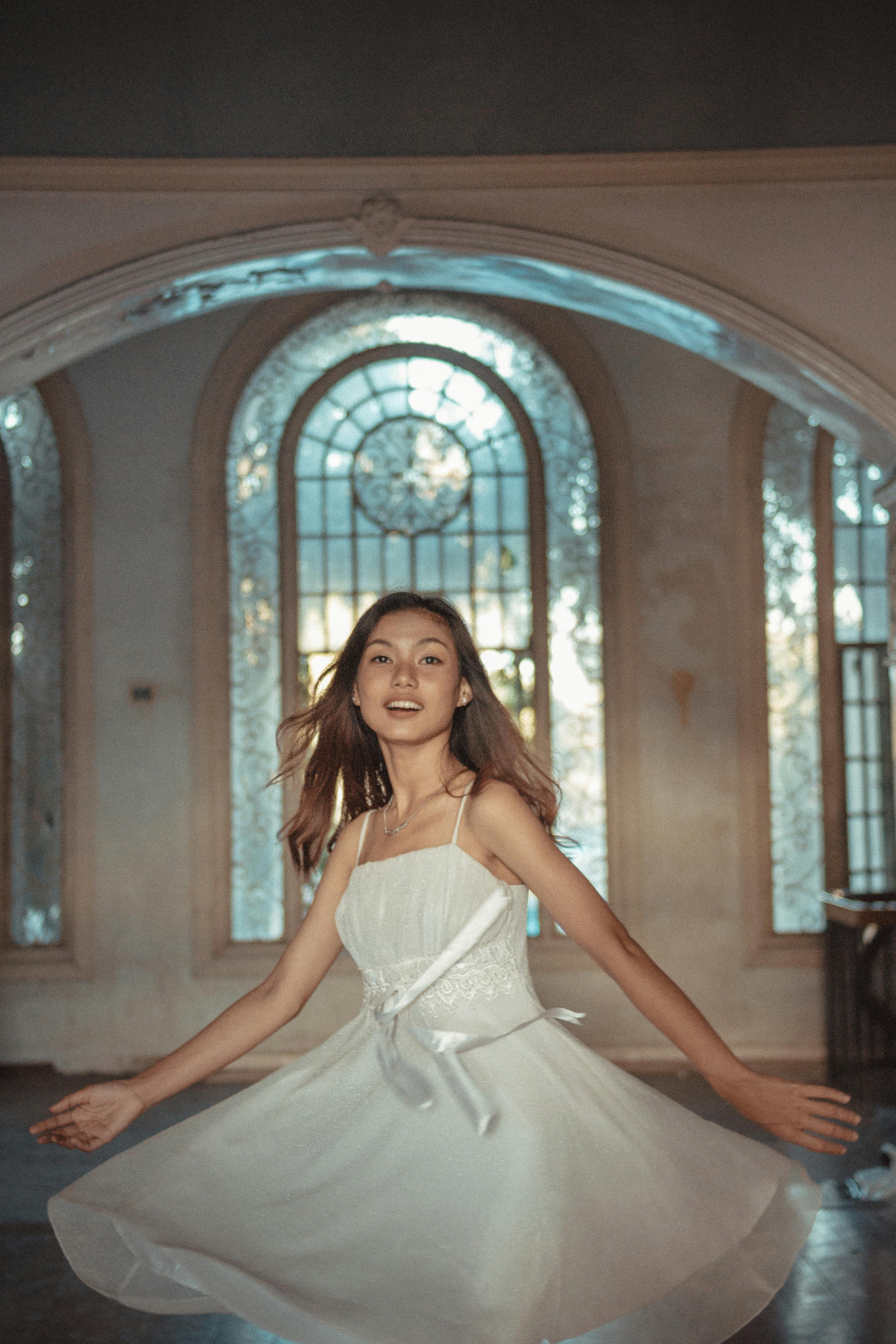 Young woman in a white dress spins joyfully inside a vintage building.
