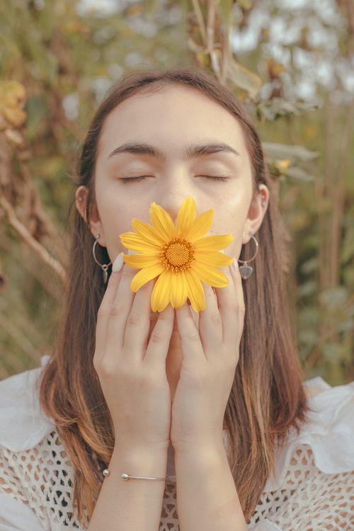Free Woman in white holds a yellow flower, eyes closed, outdoors in serene nature. Stock Photo