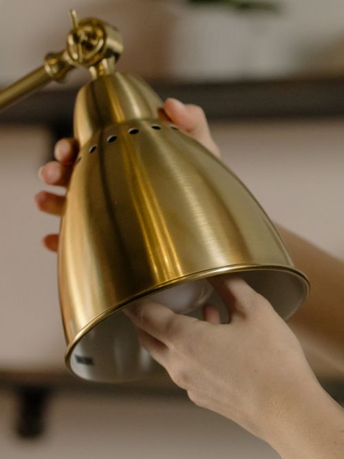 Free Close-up of hands fixing a light bulb into a modern brass desk lamp, showcasing home maintenance. Stock Photo