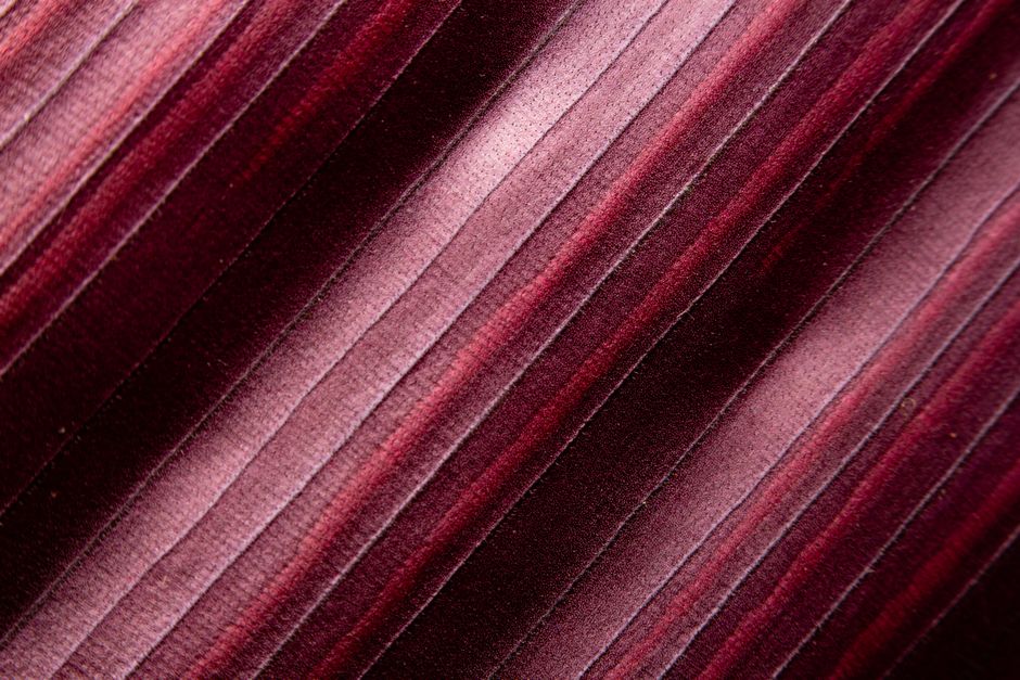 A close-up of a velvet plum-colored armchair styled with a gold floor lamp and a green houseplant