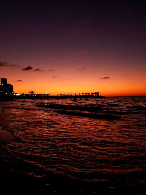 Free Amazing scenery of bright sundown sky over waving sea and silhouette of city on beach Stock Photo