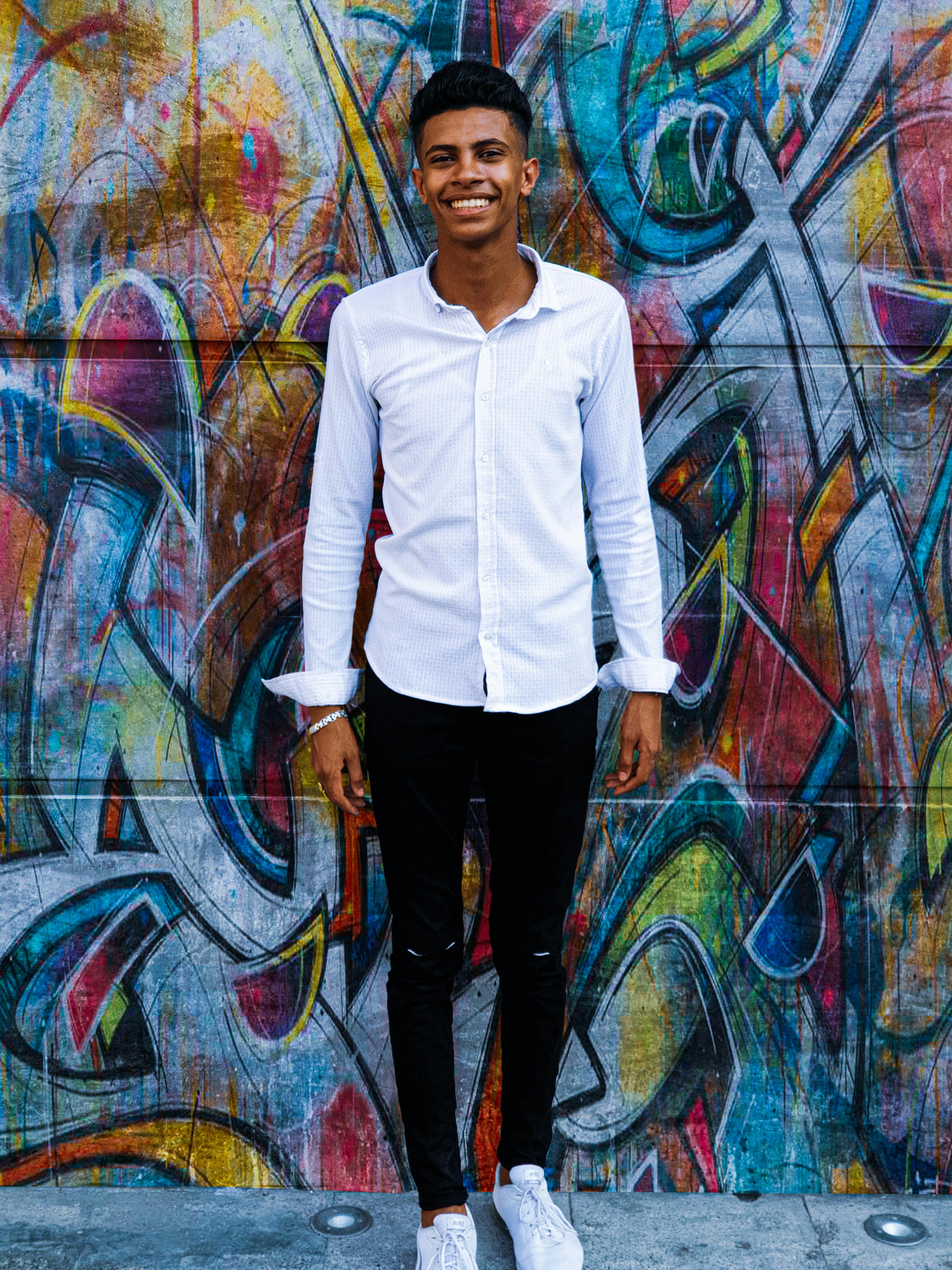 Smiling young man poses in front of a colorful urban graffiti mural, creating a vibrant portrait.