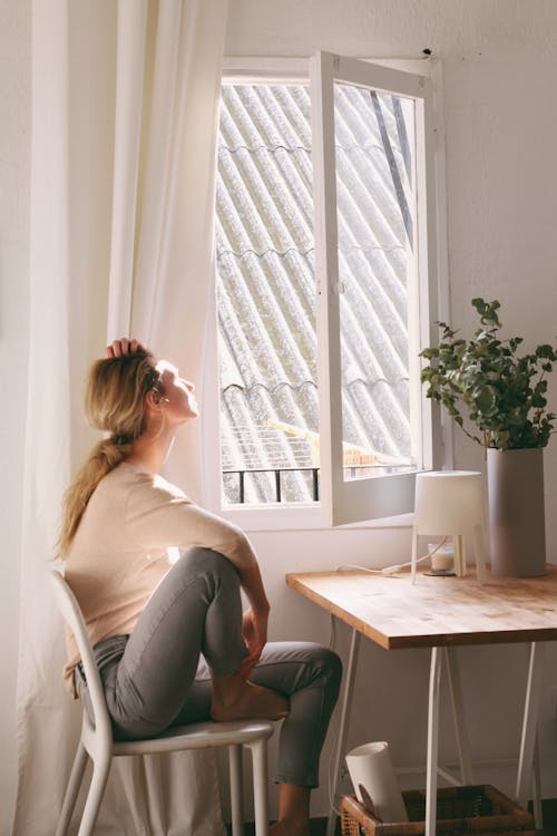 Free Woman Sitting on a Chair next to a Window Stock Photo