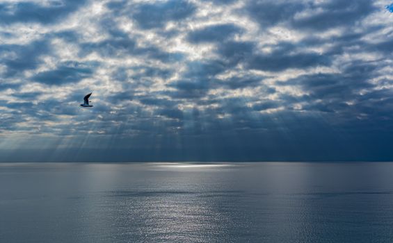 A tranquil seascape with sun rays piercing through clouds over a calm ocean.