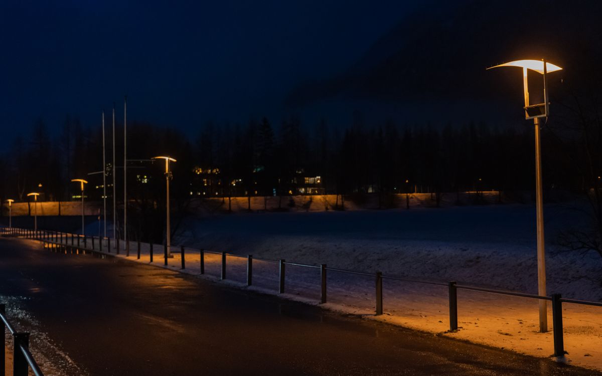 Street lamps illuminate a deserted snowy road at nighttime, creating a moody winter scene.