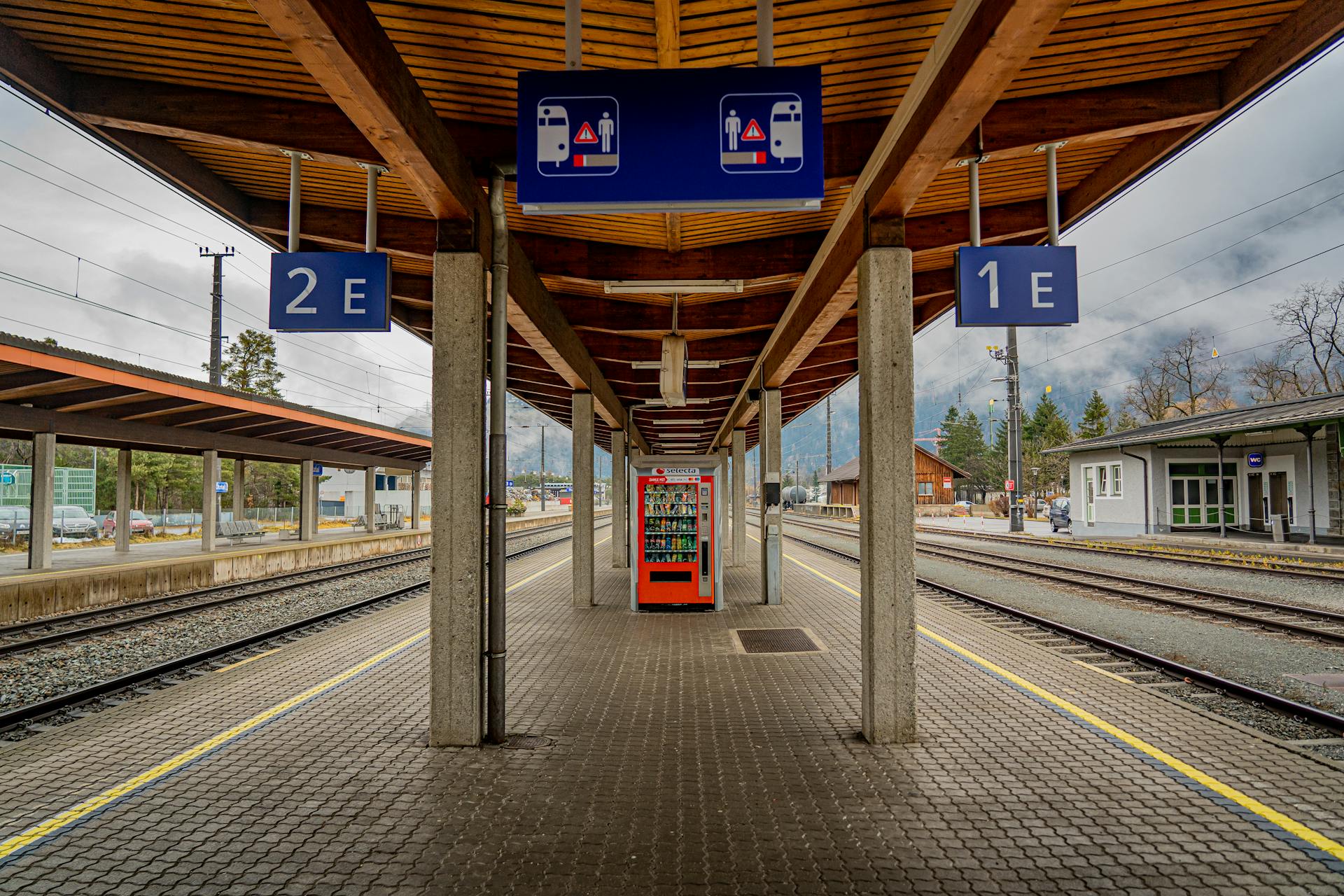 Empty train station platform featuring a vending machine and signs on a cloudy day.