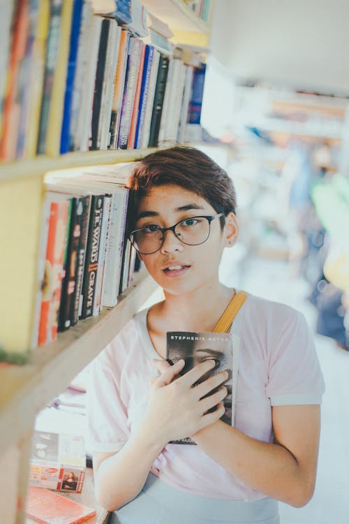 Boy in White Shirt Wearing Black Framed Eyeglasses Holding a Book