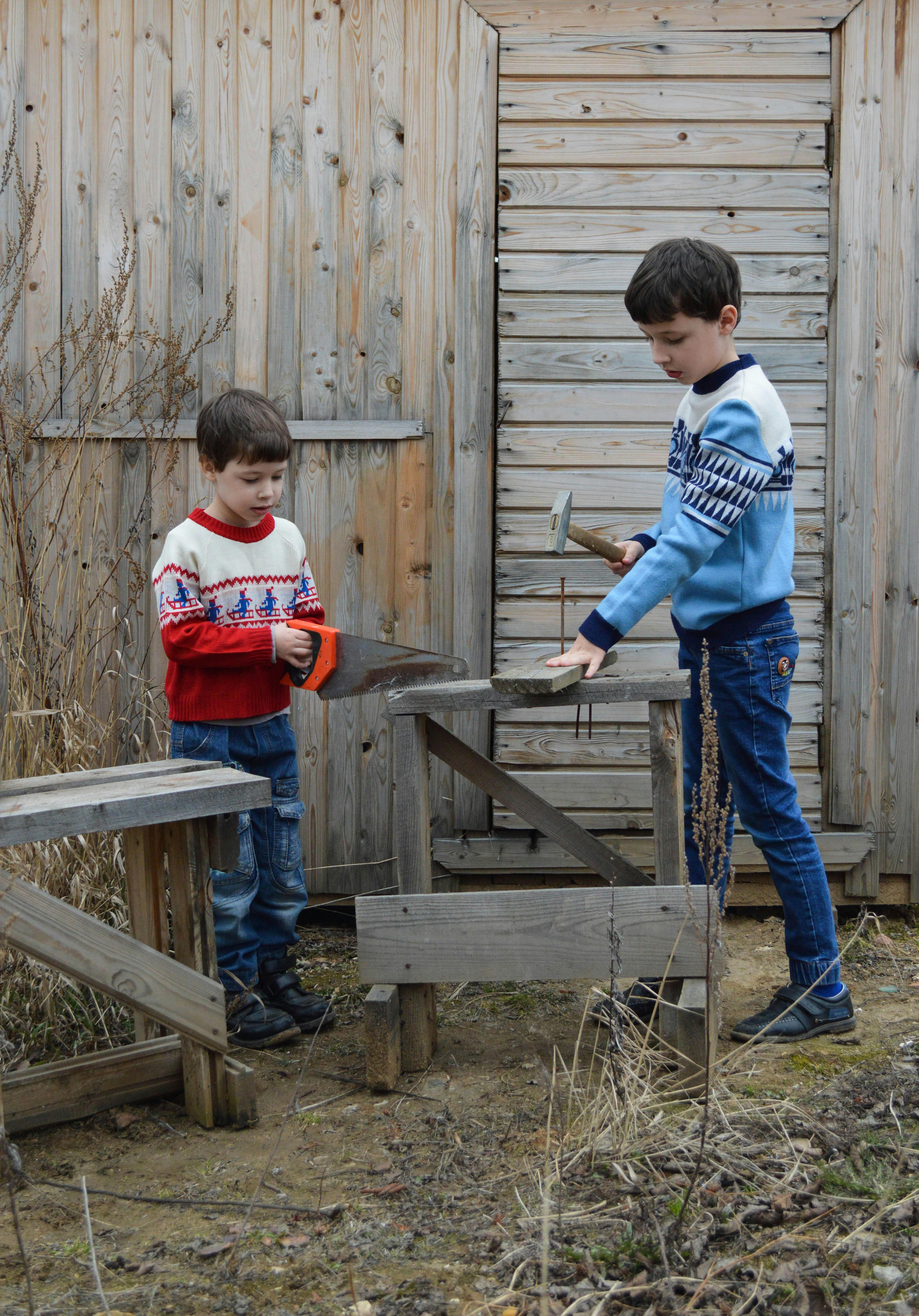 boys sawing wooden plank in backyard