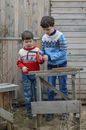 Full body of concentrated boy in warm sweater and jeans teaching focused younger brother how to saw wooden plank properly