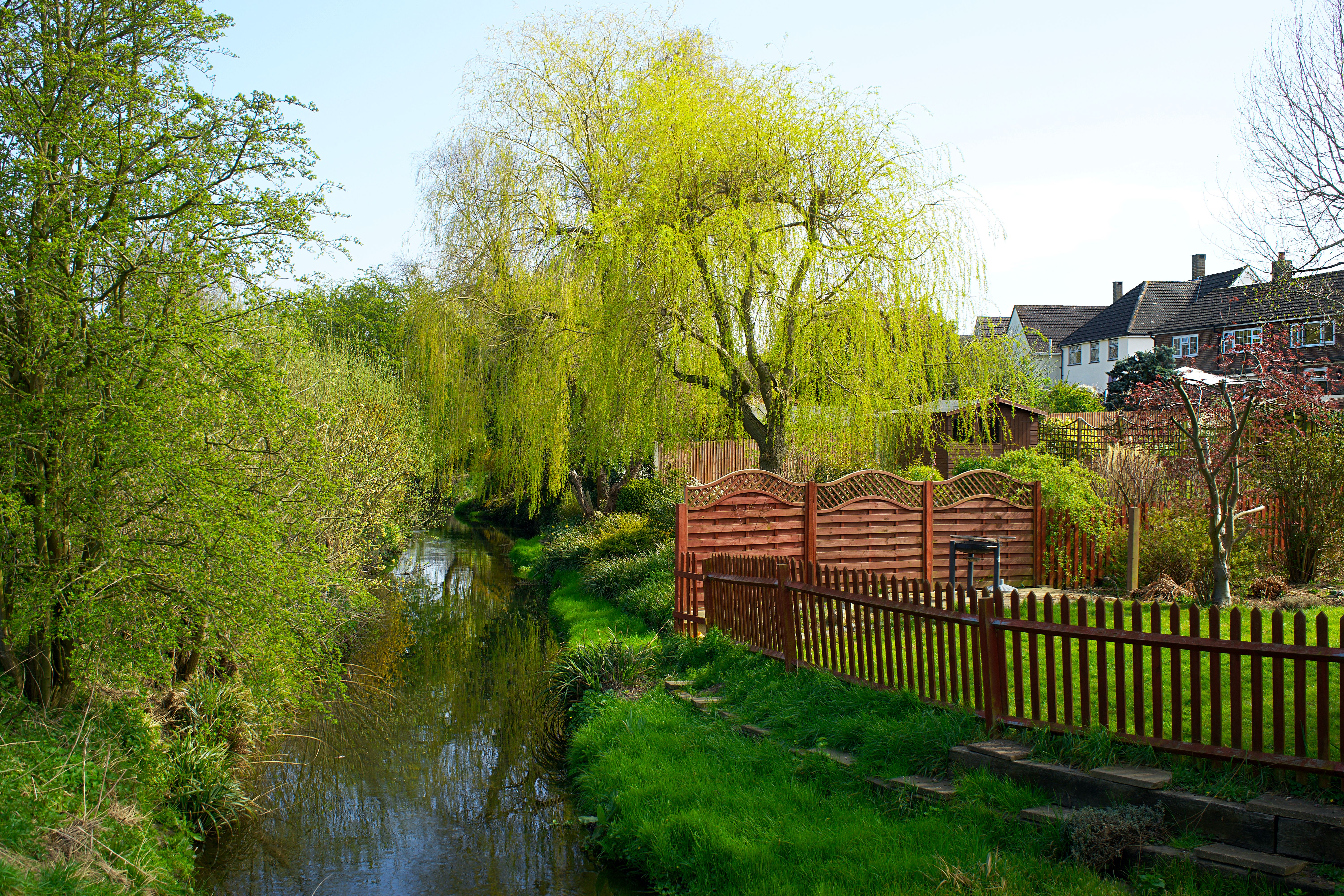 Serene spring landscape with stream, wooden fence, and lush greenery in the UK.