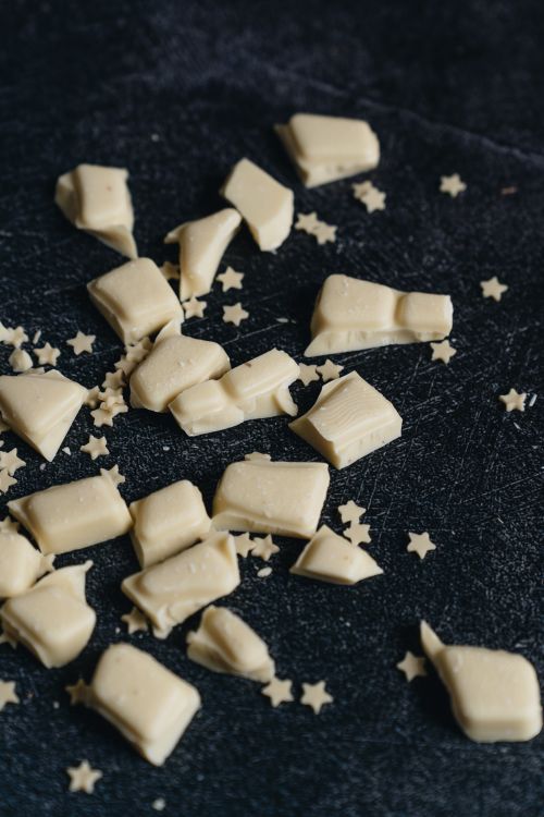 Free Close-up of white chocolate pieces on a dark textured background with star sprinkles. Stock Photo